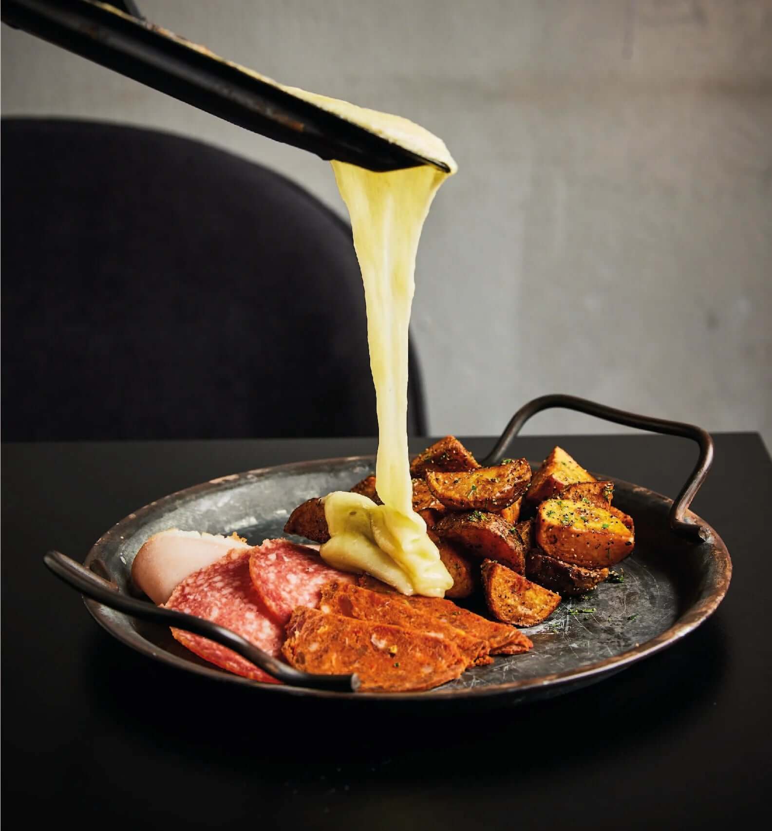 A plate featuring meat and potatoes, with cheese being poured generously over the top.