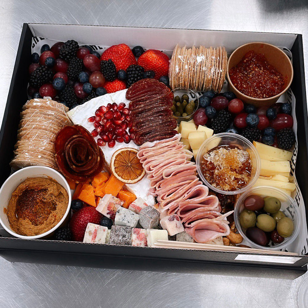 A black box with assorted cheeses, crackers, meats, fruits, and dips.