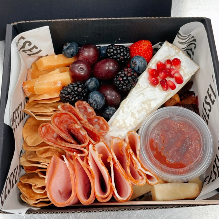A black box with assorted food including cheese, crackers, berries, and meat